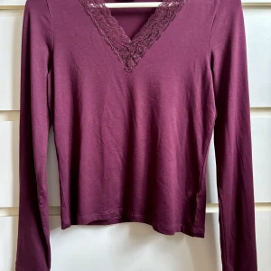 Vinröd långärmad topp med spetsdetaljer stl 170 - Säljer en vinröd långärmad topp från H&M med v-ringning och spetsdetaljer runt halsen. Perfekt för en stilren look.