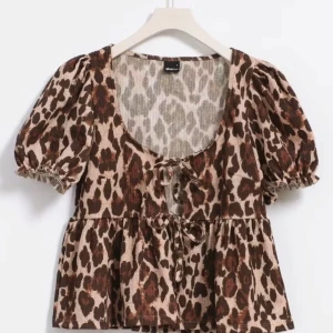 Leopardmönstrad blus med knyt - Trendig leopardmönstrad blus från Gina Tricot med korta puffärmar och knyt framtill. Den har en luftig passform och är perfekt för att ge en djärv touch till din outfit.