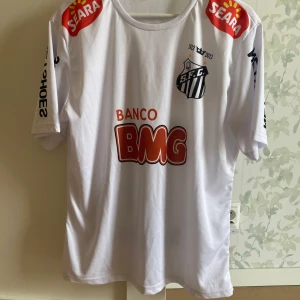 Vit fotbollströja från S.F.C. - Säljer en vit fotbollströja från Santos( inte official). Tröjan har tryck av sponsorer som Banco BMG och Seara, samt spelarens namn och nummer på baksidan. Storleken är XL men sitter mer som L. 