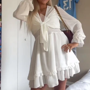 Vit dressy klänning  - Säljer en söt vit klänning med volanger och knytning framtill. Klänningen har långa ärmar och en v-ringad design. Perfekt för studenten eller sommarens alla tillfällen🌸 klänningen heter Lina dress