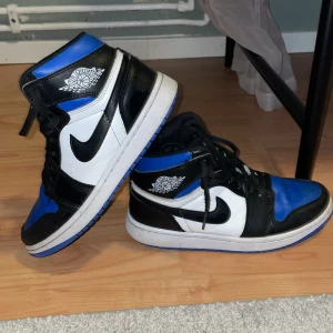 Nike Air Jordans i svart, vit och blå. - Säljer ett par Nike Air Jordans i en snygg kombination av svart, vit och blå. Skorna har den klassiska Air Jordan-loggan på sidan och en blå sula. Perfekta för dig som vill ha en stilren och sportig look.