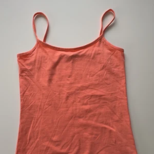 Orange linnetopp - Säljer en snygg orange linnetopp med smala axelband. Perfekt för varma sommardagar eller som ett lager under en tröja. Toppen är tillverkad i ett mjukt och bekvämt material. Aldrig använd. Har inte justerbara band
