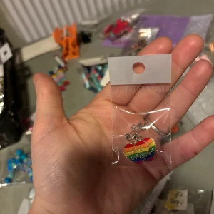 Regnbågsfärgat hjärthalsband - Säljer ett färgglatt halsband med ett hängsmycke i form av ett hjärta i regnbågens färger. Perfekt för att lägga till en pop av färg till din outfit!