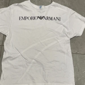 Vit t-shirt från Emporio Armani - Säljer en stilren vit t-shirt från Emporio Armani med deras ikoniska logga tryckt på bröstet. Perfekt för en avslappnad och trendig look. T-shirten har en klassisk passform och är kortärmad.