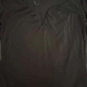Grå långärmad topp - Säljer en stilren grå långärmad topp med rynkdetaljer vid halsringningen. Perfekt för en enkel och elegant look. Passar bra till både jeans och kjol.