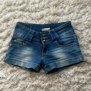 Lågmidjade jeansshorts  - Snygga blå jeansshorts med tre knappar framtill och klassisk femficksdesign. Perfekta för en avslappnad sommarlook. De har en lätt slitning för en trendig touch.