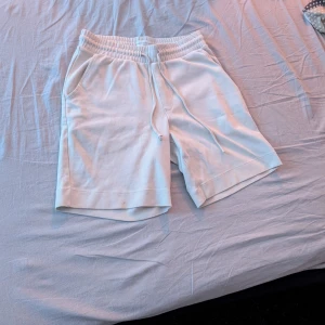 Vita shorts från These Glory Days - Snygga vita shorts från These Glory Days med elastisk midja och snörning. De har två sidofickor och två bakfickor, perfekta för en avslappnad stil. Tillverkade i ett mjukt material som ger en bekväm passform.