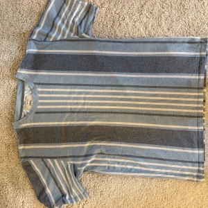 Randig t-shirt från Redefined Rebel - Säljer en snygg randig t-shirt från Redefined Rebel i blå och grå nyanser. T-shirten har korta ärmar och en klassisk passform. Perfekt för en avslappnad stil. Storlek M. Mycket bra skick