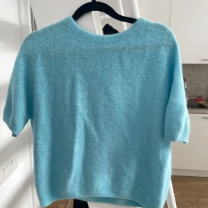Ljusblå stickad tröja - Säljer en ljusblå stickad tröja med korta ärmar. Perfekt för en avslappnad stil och passar bra till både jeans och kjol. Tröjan har en rund halsringning och är mjuk och bekväm att bära. Äkta ull 
