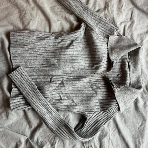 Grå ribbad tröja med krage - Säljer en stilren grå ribbad tröja med krage och långa ärmar. Perfekt för en avslappnad men ändå snygg look. Tröjan har en klassisk design som passar till många olika outfits.