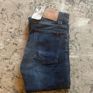 W 26 L29 Mörkblå jeans från Nudie Jeans - Snygga mörkblå jeans från Nudie Jeans med en klassisk femficksdesign. Jeansen har en slim passform och är tillverkade i högkvalitativt denim. Perfekta för en stilren look.