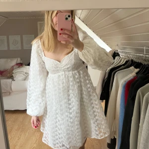 Vit blommig klänning från NA-KD - Säljer en söt vit klänning från NA-KD med blommigt mönster och långa ärmar. Klänningen har en v-ringad design och är perfekt för vår och sommar. Perfekt för en solig dag eller en speciell tillställning. 💞💞(lite smutsig på några blommor, syns inte när klänningen är på)