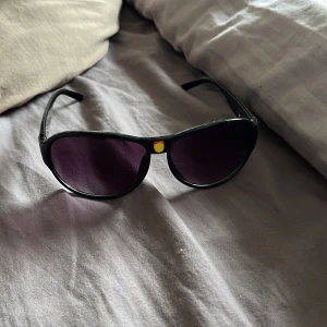 Svarta solglasögon med gul detalj - Snygga svarta solglasögon med en unik gul detalj på framsidan. Perfekta för soliga dagar och ger en cool look. De har en klassisk form och mörka glas.