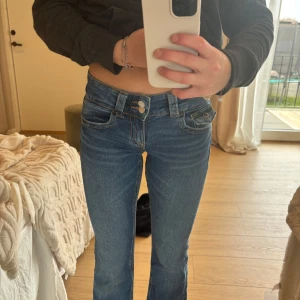 Blå jeans från Gina Tricot - Säljer ett par snygga blå jeans från Gina Tricot. De har en låg midja och en tight passform med klassisk femficksdesign. Jeansen har dubbla knappar och dragkedja framtill. Perfekta för en avslappnad stil.