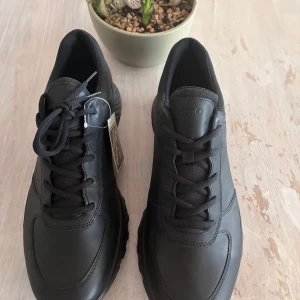 Svarta sneakers från Ecco - Snygga och stilrena svarta sneakers från Ecco. Skorna har en klassisk design med snörning och en bekväm sula med gul detalj. Perfekta för en avslappnad stil.