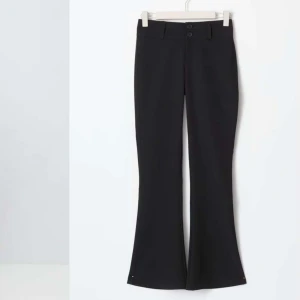 Svarta bootcut kostymbyxor - Snygga svarta kostymbyxor med bootcut-stil och hög midja. Byxorna har två knappar framtill och är perfekta för en stilren look. Passar utmärkt till både vardag och mer formella tillfällen.