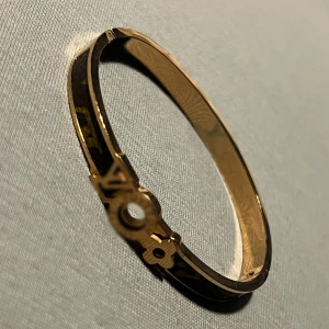 Guldarmband med dekorativt lås - Elegant guldarmband med ett unikt dekorativt lås. Armbandet har en slät och glänsande yta som ger en lyxig känsla. Perfekt för att ge en stilfull touch till din outfit.