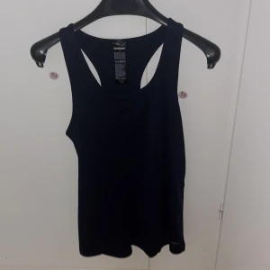 Mörkblå  linnetopp från Newbody - Säljer en stilren svart linnetopp från Newbody i storlek S. Perfekt för träning eller en avslappnad dag. Tillverkad i ett mjukt och bekvämt material med en klassisk design. Aldrig använd