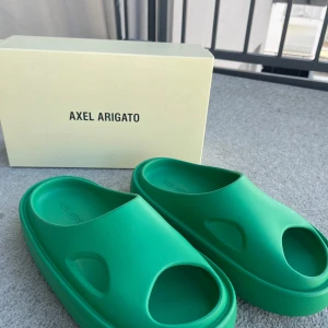 Gröna sandaler från Axel Arigato - Oanvända och snygga gröna sandaler från Axel Arigato med öppen tå och en stilren design. Perfekta för sommarens varma dagar eller som innetofflor. Sandalerna har en robust sula för extra komfort.    Nypris: 2600kr