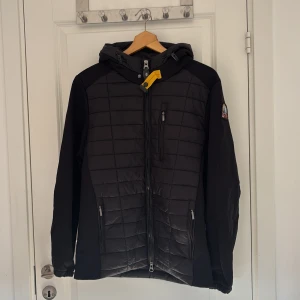 Parajumpers jacka - Säljer en svart jacka från Parajumpers med dragkedja och huva. Jackan har ett märke på ärmen och är designad för extrema förhållanden. Perfekt för kyligare väder med sin quiltade stil och praktiska fickor.