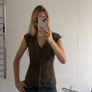 Gröna populär topp från weekday - Säljer en stilren grön ärmlös topp från Weekday. Toppen har en v-ringad design och knäppen framtill. Supersnygg och eftertraktad. Endast använd några gånger!