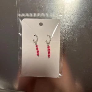 Silvriga örhängen med rosa pärlor - Snygga silvriga örhängen med hängande rosa pärlor. Perfekta för att ge en färgklick till din outfit. De har en enkel och elegant design som passar till många tillfällen.