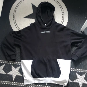 Svart och vit hoodie med text - Säljer en svart och vit hoodie med texten 'STAY COOL' på bröstet. Den har en stor ficka framtill och en bekväm huva. Perfekt för en avslappnad stil.