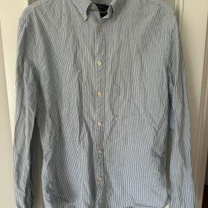 Randig Oxfordskjorta från East West - Snygg randig button-down Oxfordskjorta från East West i blått och vitt. Skjortan har långa ärmar och knappar framtill. Perfekt för en stilren look.