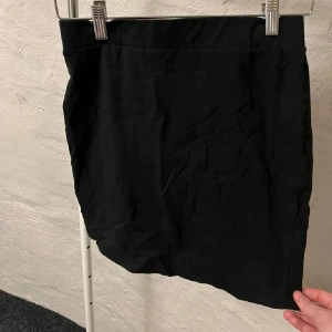 Svart kortkjol - Snygg svart kortkjol perfekt för olika tillfällen. Enkel design som gör den lätt att matcha med olika toppar. Ett måste i garderoben för en stilren look.