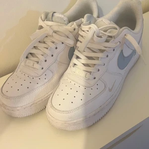 Vita Nike Air Force sneakers - Säljer ett par klassiska vita Nike Air Force sneakers med ljusblå swoosh. Skorna har snörning och perforerade detaljer på tån för ventilation. Perfekta för vår/ sommar. Endast använt tre gånger! 🤩👌🏻(pris kan diskuteras)