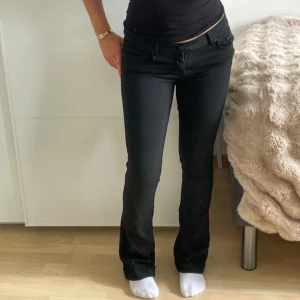 Svarta bootcut jeans - Snygga svarta bootcut jeans med låg midja. Perfekta för en stilren look. De har en klassisk design med dragkedja och knappar framtill. Slitna längst ner men inget som man märker av