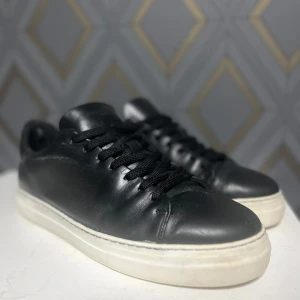 Svarta sneakers från Selected Homme - Snygga svarta sneakers i skinn från Selected Homme. De har en klassisk design med svarta snören och en vit sula. Perfekta för en stilren look.