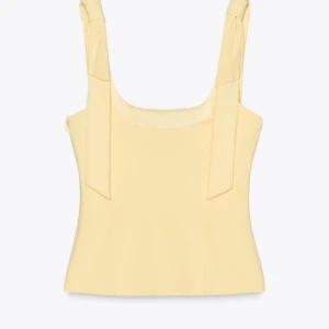 Gul korsettopp med knytband - Snygg gul korsettopp med breda axelband som knyts i rosetter. Toppen har en figurnära passform och är perfekt för sommarens varma dagar. 💛