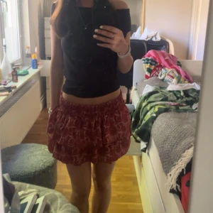 Röd kortkjol med mönster - Säljer en röd kortkjol med ett subtilt mönster. Kjolen har en elastisk midja för bekväm passform. Perfekt för varma dagar!