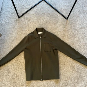 Olivgrön overshirt från Samsøe Samsøe - Snygg olivgrön overshirt från Samsøe Samsøe med dragkedja och en bröstficka. Perfekt för en stilren look.