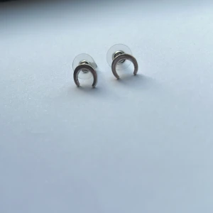 Silverfärgade örhängen i halvmåneform - Säljer ett par stilrena silverfärgade örhängen i form av halvmånar. Perfekta för att ge en subtil men elegant touch till din look. De är små och lätta, vilket gör dem bekväma att bära hela dagen.