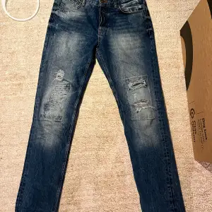 Säljer ett par snygga och unika blå jeans från Adrian Hammond Hollywood i storlek W32 men sitter mer som en 31. passformen är straight fast mer åt slim hållet. De har en cool slitning på framsidan och en klassisk femficksdesign. Perfekta för en avslappnad stil eller en utekväll. Tveka inte på att höra av er för frågor och funderingar:)