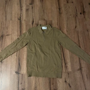 Brun långärmad tröja med dragkedja - Säljer en stilren brun långärmad tröja från Selected Homme med dragkedja vid halsen. Perfekt för en avslappnad men ändå snygg look. Tröjan har en klassisk krage och ribbade muddar vid ärmslut och nederkant.