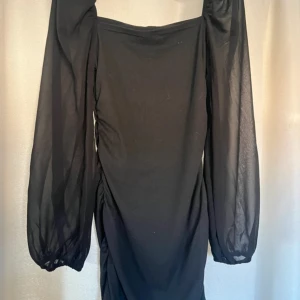 Svart klänning med långa ärmar - Elegant svart klänning med långa, transparenta ärmar och fyrkantig urringning. Perfekt för en stilren look.