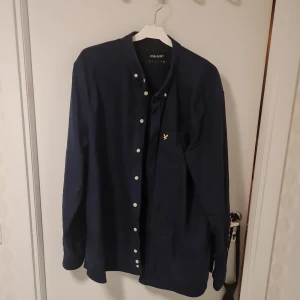 Mörkblå skjorta från Lyle & Scott - Säljer en stilren mörkblå skjorta från Lyle & Scott. Skjortan har långa ärmar och knappar framtill. Tillverkad i 100% bomull för en bekväm känsla. Perfekt för en avslappnad men ändå uppklädd look.