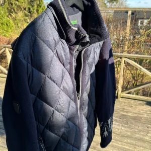 Mörkblå cardigan jacka - Säljer en snygg mörkblå vardigan jacka med dragkedja och ribbade detaljer. Jackan har långa ärmar med ett diskret mönster längst ner på armen. Pm vid funderingar!