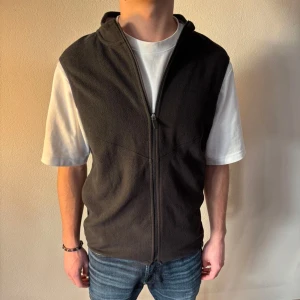 Svart fleeceväst med dragkedja - Snygg svart fleeceväst med dragkedja framtill. Perfekt för lager-på-lager under kyligare dagar. Västen har en normal passform och är idealisk för både vardag och utomhusaktiviteter.