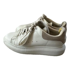 Vita sneakers från Alexander McQueen - Säljer ett par stilrena vita sneakers från Alexander McQueen. De är tillverkade i skinn med detaljer i grå mocka på hälen. Fint skick och boxen finns att få. Köpta från vestriare där dom även genomgått kontroll för att vara äkta. Pris går att diskutera