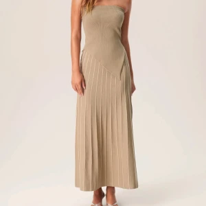 Beige ribbad långklänning - Elegant beige långklänning med ribbad struktur och asymmetrisk design. Klänningen har en smickrande passform och är perfekt för en stilren look.