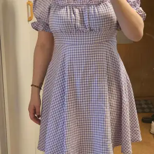 Charmig lila rutig klänning med puffiga kortärmar och en smickrande passform. Perfekt för en somrig look med sin söta design och bekväma material. Oanvänd