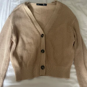 Beige stickad kofta från 157 - Säljer en beige stickad kofta från 157 med v-ringning och stora knappar framtill. Koftan har långa ärmar och ribbade kanter som ger en snygg passform.🤍