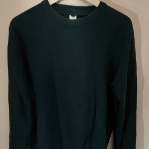 Mörkgrön tröja från Visual Clothing Project - Säljer en stilren mörkgrön tröja från Visual Clothing Project. Tröjan har en klassisk rund hals och långa ärmar, perfekt för kyligare dagar. Den är tillverkad i ett mjukt material som ger en bekväm passform. (Liten hål under armhålan men syns inte under användning). Passar medium också