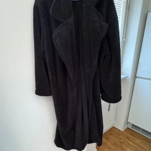 Svart teddyjacka - Mysig svart teddyjacka med lång passform och stora slag. Perfekt för kyliga dagar när du vill hålla dig varm och stilren. Jackan har en mjuk och fluffig yta som ger en skön känsla.