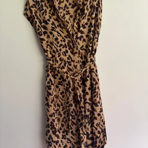 Leopardmönstrad klänning från Pieces - Snygg leopardmönstrad skjortklänning från Pieces i beige och bruna toner. Klänningen kan bäras öppen till jeans och top eller stängd med ett knytband i midjan. Viskos 100% använd två gånger.