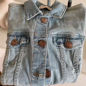 Ljusblå jeansjacka från Camaïeu - Snygg ljusblå jeansjacka från Camaïeu med klassisk krage och knappar framtill. Jackan har två bröstfickor med knappdetaljer och långa ärmar. Perfekt för en avslappnad stil. Anänd 2-3 gånger, som ny. Tvättad. Djurfritt och rökfritt hem.